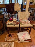 Overall view of assorted table linens, throw blankets, doilies, napkins, and napkin holders arranged on and around chairs