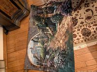 Full view of tapestry laid flat showing garden path, flowers, arched stone bridge, and buildings beyond, with hanging hardware visible at the top.