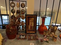 Wide view of the lot showing various vases, figurines, votive holders, and wall art arranged on a table and in front of decorative metal wall hanging.