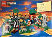 Front cover of the LEGO instruction manual featuring a completed pirate-themed LEGO set with ships, palm trees, towers, and minifigures under a sunset sky.