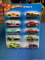 Photos showing the front and angled views of the sealed 10-pack Hot Wheels cars. The pack contains 10 colorful collectible die-cast car models in blue cardboard and plastic blister packaging, with 'New' label visible.