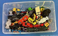 Top-down photo of a large plastic bin filled with assorted Hot Wheels toy cars including race cars, trucks, and a helicopter in multiple colors.