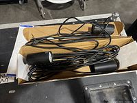 Three black display lights in a cardboard box with long power cords coiled inside.