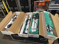 Eight Lightcraft fluorescent display light fixtures packed in cardboard boxes, cords and tubes attached or included, shown laying on a large black case.