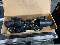 Two black ribbed skandalights spotlights with attached power cords inside a cardboard box
