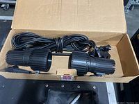 Two black Skandalight spotlights in a cardboard box with attached cords and lamps