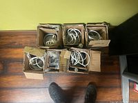 Six cardboard boxes each containing pendant light parts including cords and metal shades.