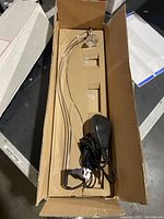 Photo showing one wire display light fixture in a box with curved wire arm, bulb socket, and black power cord end.