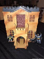 Front view of the Batman-themed plastic house playset with two Batman figurines positioned on either side.