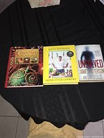 Three books laid side by side on a black cloth: The Ultimate Christmas Reader's Digest, Home Style Cookery, and Unsolved by James Patterson and David Ellis.