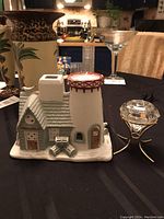 Side view of the ceramic winter house candle holder and lead crystal candle holder on the table with kitchen background.