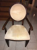 Front view of the wooden chair with beige upholstered round backrest and seat cushion describing overall design and wear.