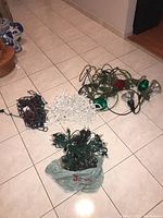 Lot of Christmas lights shown on floor including green and white cord light strands and outdoor flood lights with colored covers.