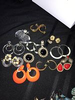 12 pairs of assorted costume costume jewelry earrings laid out on black fabric, different shapes and colors including hoops, studs and drops.