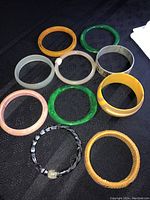10 assorted costume jewelry bracelets including plastic/resin bangles in various colors and styles plus corded bracelet.
