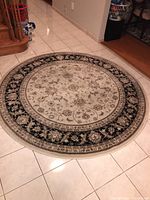 Photo showing full round beige and black area rug on a tiled floor.