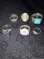 Photo showing six silver rings arranged on black textured fabric showcasing various designs and stones including amethyst and turquoise.