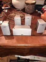 Five Sony speakers on a brown surface: four small bookshelf speakers and one horizontal center channel speaker.