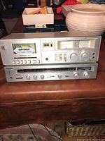 Two silver Technics stereo components stacked: top is RS-M205 cassette player with VU meters and soft-touch button controls, bottom is SA-103 stereo receiver with tuning dial and control knobs