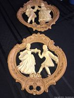 Two sculptured wall plaques with dancing couple figures and ornate carved wooden frames.