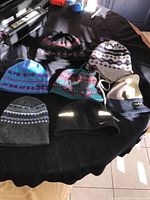 View of all 7 winter toques laid on a black surface showing different colors, patterns, and brands including Nike, Chaos, and Sunice.