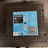 Top view of black plastic pegboard with blue label showing brand, measurements, and load capacity.