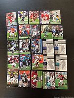 Top-down view of 22 football cards laid out in five rows on a dark surface, showing the front of the cards with various NFL players in action.