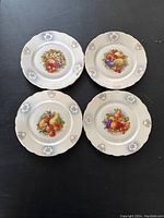 Four round porcelain soup bowls arranged together showing fruit patterns in the center and decorative borders.