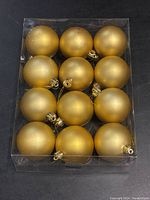 Top view of 12 gold matte finish Christmas ball ornaments in a clear plastic box.