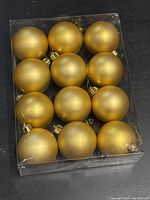 Top view of 12 gold matte Christmas ball ornaments arranged in a clear plastic box, showing smooth and uniform finish.