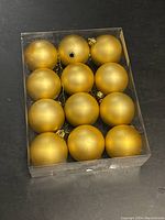 Top view of 12 gold ball ornaments in a clear plastic box, showing all spheres tightly packed in rows.