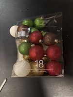 Photo showing 18 shatterproof Christmas ball ornaments in multiple colors with glitter finish packaged together.