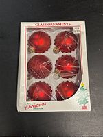 Full set of six red glass Christmas ball ornaments in original box with plastic cover. Three have ribbed edges, two smooth finish, one glittered finish.