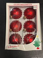 Two packages of red glass ball Christmas ornaments with scalloped edges, six ornaments per package in original packaging.
