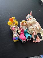 Three clown dolls laid on a flat surface showing full body, detailing the costume colors and facial features.