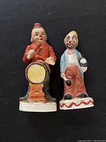 Both clown figurines together on black background showing overall condition and size comparison.