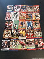 Photo of a collection of 17 football trading cards laid out on a black surface showing various NFL players in action poses or team photos.