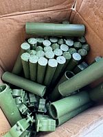Box filled with multiple green plastic plant stakes with hollow interiors and textured wood-like exterior.