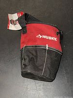 Front view of Husky utility sack bag showing red and black fabric with white Husky logo and attached product tag.