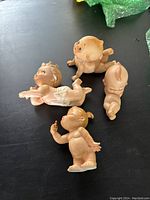 Four pink bisque Kewpie baby figurines arranged on a dark surface, showing different poses and facial expressions.