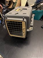 Side angle showing the gray plastic pet carrier with beige metal wire door and ventilation.