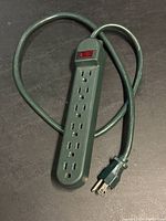 Full view of the green power strip laid flat showing six outlet holes and attached cord with plug.