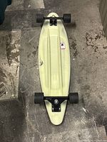 Top view of the skateboard showing the underside with wheels and trucks. The color is off-white and wheels are black.