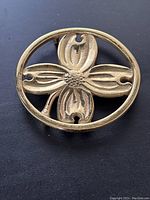 Front view of the brass trivet showing the dogwood leaf design inside a circular frame.
