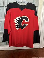 Front view of the Calgary Flames hockey jersey showing the red body with black shoulders and sleeves, and the large flaming C logo embroidered on the chest.