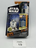 Two images showing two sealed Hasbro Star Wars Saga Legends R2-D2 figures from 2010, in original packaging with batteries included and Galactic Battle Game info on card back.