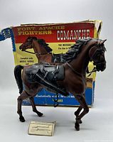 Brown plastic horse figure from the front with saddle, bridle, and part of original box visible behind.