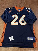 Front view of the navy blue Denver Broncos jersey with number 26 and 'Broncos' text on chest, including orange side panels and large white numbers.