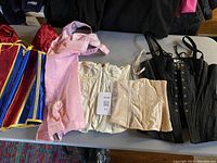 Top view of five corsets and bustier pieces laid out on table showing colors and styles including Snow White themed, pink vintage, cream, nude, and black corsets