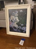 Full view of the framed floral artwork placed on the floor showing white cosmos flowers and a butterfly on a dark background
